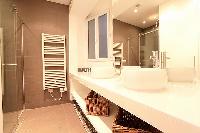 spacious bathroom with double sinks, bathroom shelves, wicker baskets, a mirror, and a shower area w