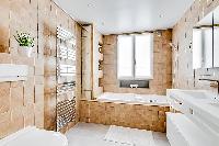 cozy bathroom in brown and white motif with a toilet, double sinks, bathroom shelves, a mirror, a ba