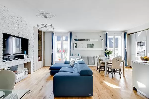 spacious living space with an L-shaped muted blue sofa, built-in shelves with decorative pieces, a t