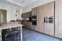 sleek kitchen with black counter tops, wooden cabinets and tall wooden table and stools in a 3-bedro