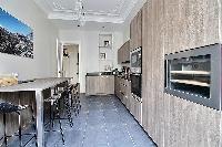 sleek kitchen with black counter tops, wooden cabinets and tall wooden table and stools in a 3-bedro