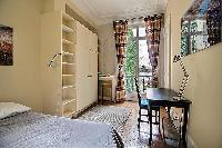 second bedroom with a queen-size bed, built-in shelves and cabinets, and a study desk with a lamp an