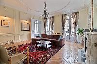 elegant living area with a brown L-shaped sofa, two armchairs, a center table, shelves, a television