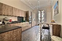 sleek kitchen with black counter tops, wooden cabinets and tall wooden table and stools in a 3-bedro