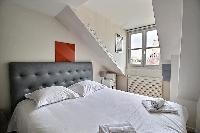 first bedroom with a queen-size bed, and a bedside table with a lamp in a 2-bedroom Paris luxury apa