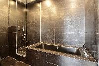 a full bathroom with an open shower, bathtub, double sink and a toilet in a 2-bedroom Paris luxury a