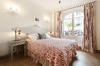 second bedroom with queen size bed, bedside tables, lamps, bright French windows and drape curtains 