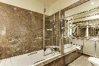 an en-suite bathroom composed of a toilet, bathtub with a handheld showerhead in a 2-bedroom Paris l