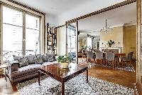 classy living area with comfortable grey sofa, wooden center table, French window, and bookshelf wit