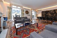 elegant living area with grey sofas,glass center table, dining area, and French windows overlooking 