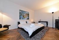 cozy bedroom with king-sized bed, parquet floor, grey carpet rug and armchair in paris luxury apartm