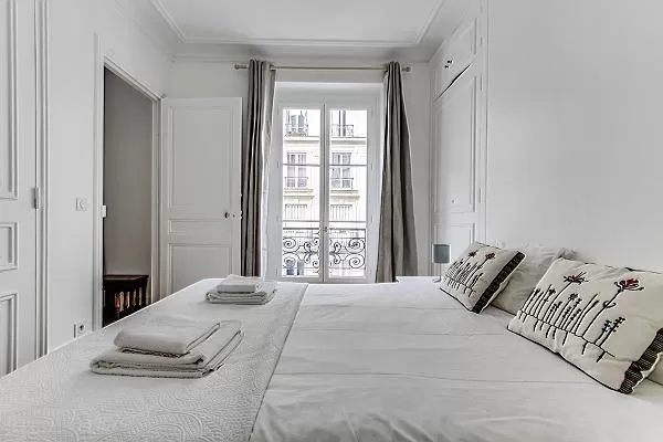 bedroom with a queen size bed and tall glass window fronting the street in paris luxury apartment