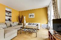 cozy living room with rich yellow walls, two Scandinavian-style double-sized sofa beds, and entertai