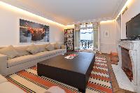 a long taupe sofa with pillows, a TV, French window, bookshelves, and ornamental fireplace  in paris