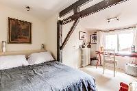 second bedroom with a queen-size bed, studytable and chair, and exposed beams in a 4-bedroom Paris l